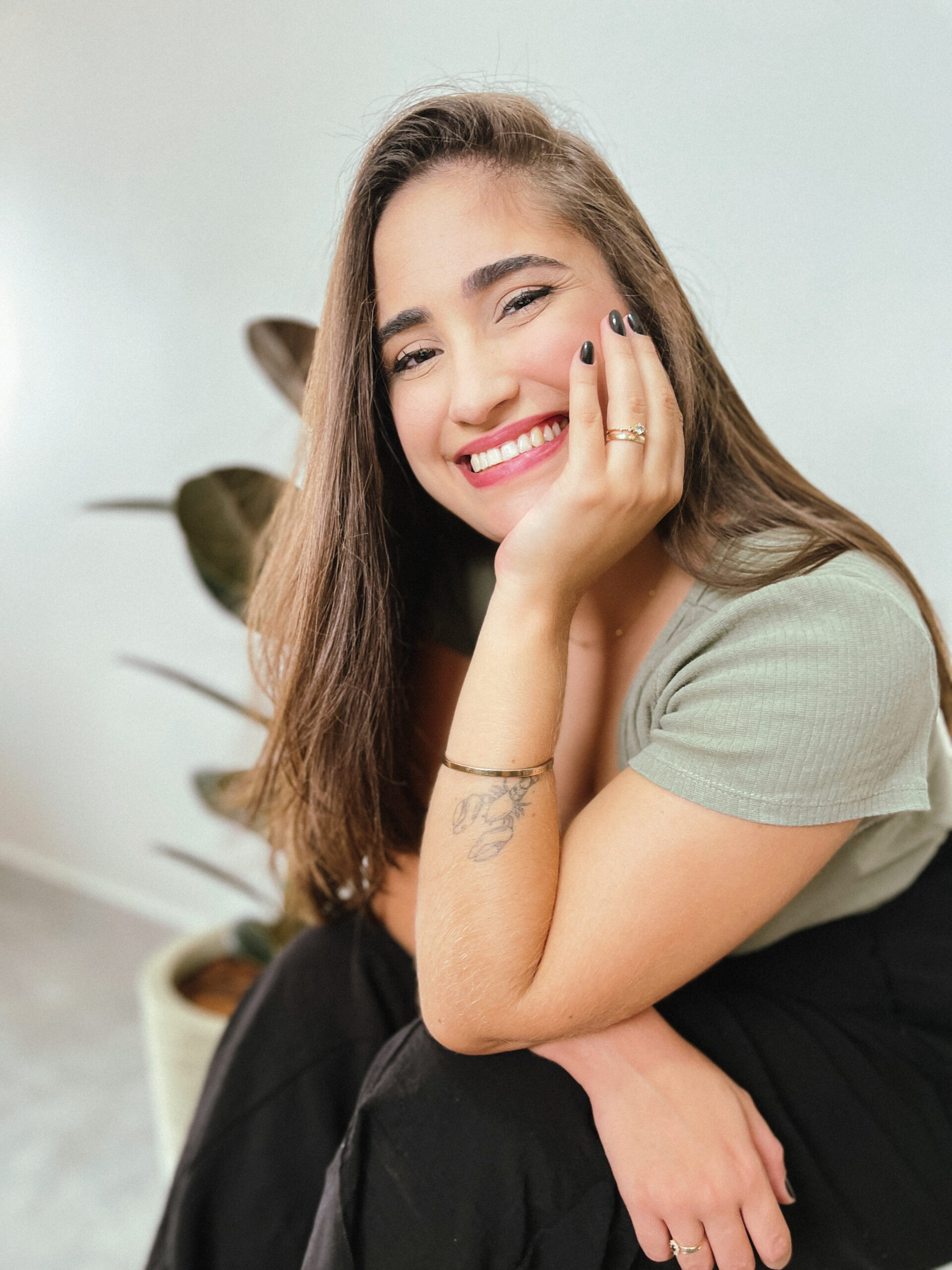 Foto de Luana morais sentada com a cabeça apoiada em uma das mãos e sorrindo